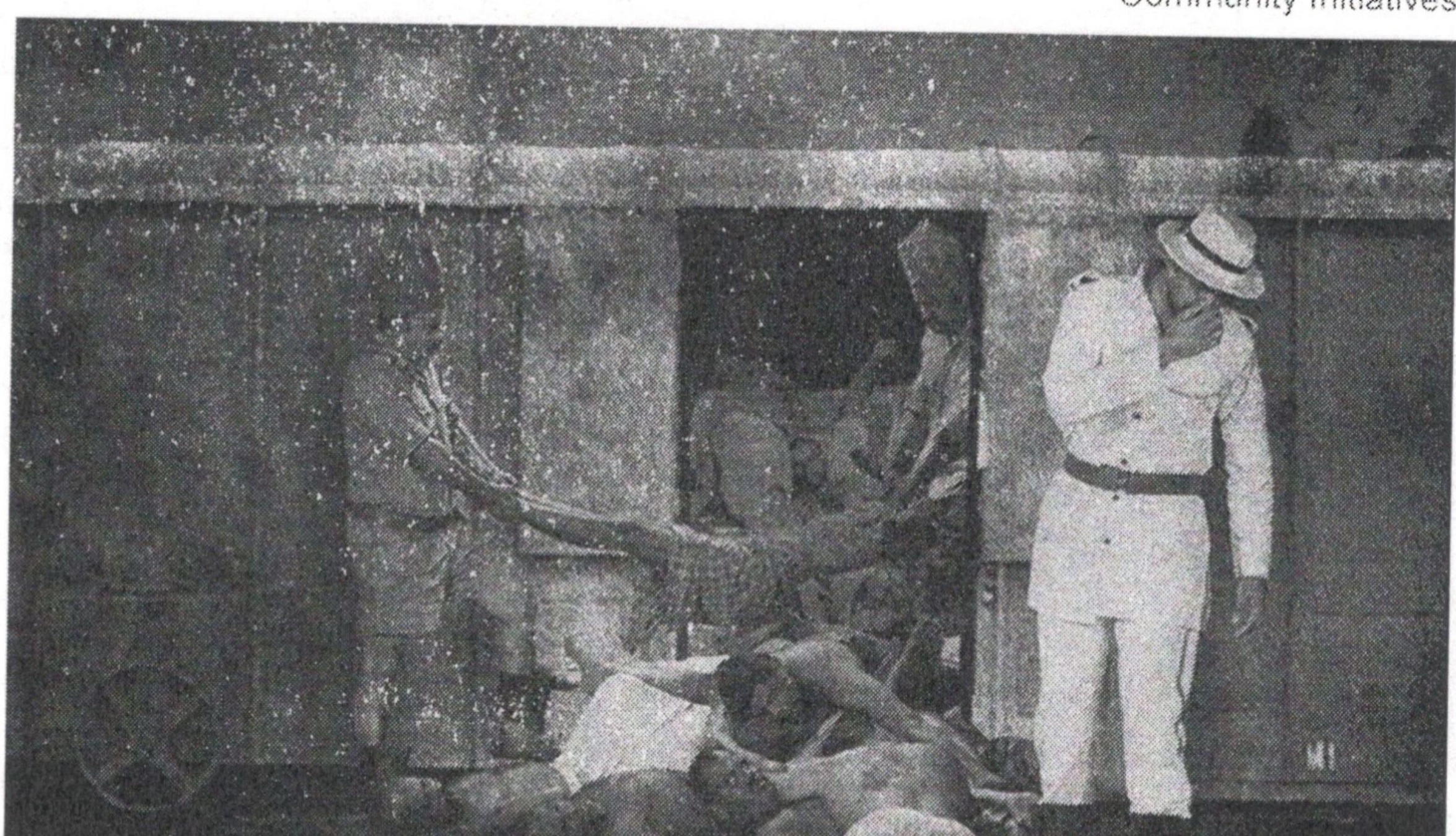 Uniformed man standing beside seated people in an archival scene